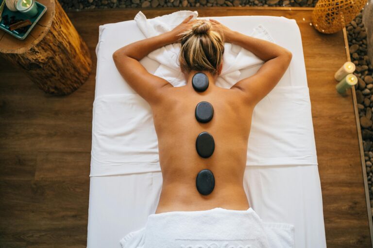 Woman lying on towel with hot stones in a serene Zen garden – luxury therapeutic massage at Zennergy spa